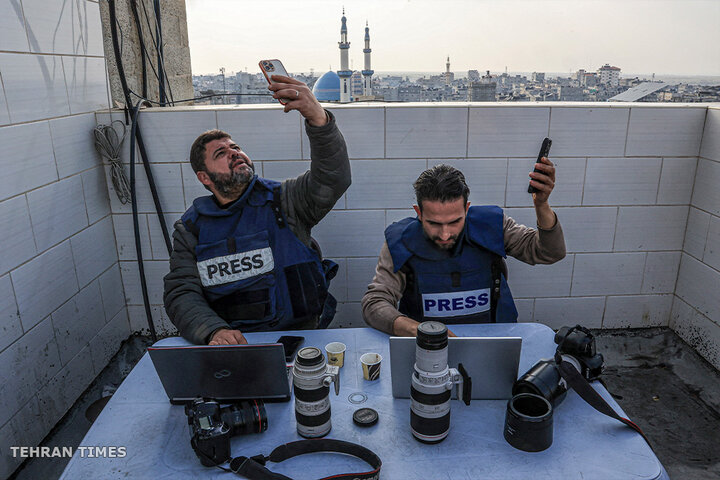 Palestinian journalists attempt to connect to the internet using their phones in Rafah on the southern Gaza Strip. [Said Khatib/AFP]

