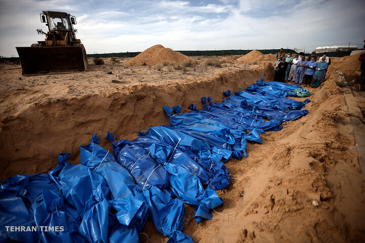 Palestinians pray over bodies of people killed in the Israeli bombardment. The bodies were brought from the al-Shifa Hospital for burying in a mass grave in the town of Khan Younis. [Mohammed Dahman/AP Photo]
