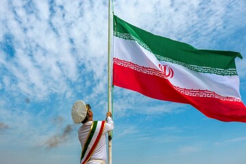 Under a brilliant, cloud-streaked sky, a ceremonial naval officer in a sharp white uniform hoists the Iranian flag on Hormuz Island on April 30, 2026, marking  the observation of National Persian Gulf Day.