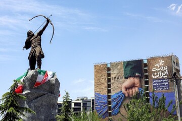 A statue of Arash the Archer, the legendary Persian hero, stands near a billboard in Tehran’s Vanak Square. The billboard depicts the Strait of Hormuz and bears the Persian slogan: “Forever in Iran’s Hand.”