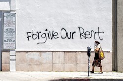 A woman wearing a mask walks past a wall bearing graffiti asking for rent forgiveness in Los Angeles on May 1, 2020. (Photo: Valerie Macon / AFP via Getty Images)