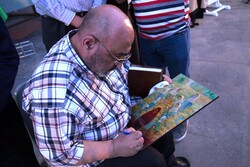 Abdolhamid Qadirian autographs a copy of his painting “Girls of the Sayed Al-Shuhada School” for a student after unveiling the original the Seyyed al-Shohada Girls’ School in Golshahr on July 18, 2021