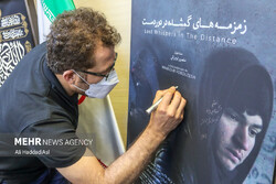 Filmmaker Mansur Foruzesh autographs a poster for “Lost Whispers in the Distance” in a meeting held in Tehran on September 18, 2021 to promote the documentary. (Mehr/Ali Haddadi-Asl)