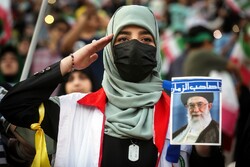 A woman holding a picture of the Leader salutes along with tens of thousands of children gathered together at Tehran’s Azadi Sports Complex to perform the anthem “Salam Commander” on May 26, 2022. (IR