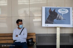 A person is seen sitting after departing from a Tehran Metro train car beside a cartoon on view in the exhibition “Cannes in Close-up” at the Vali-e Asr subway station on June 6, 2022. (YJC/Zahra-Sada