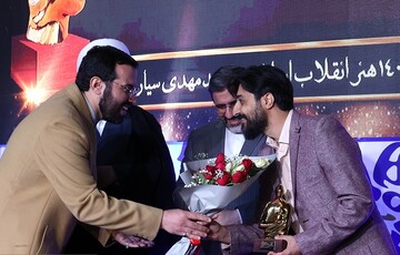 Songwriter Mohammad-Mehdi Sayyar (R) accepts a bouquet of flowers from Art Bureau deputy director Ali Foruzanfar after being named the Eternal Figure of Revolutionary Art in Tehran on April 16, 2023.