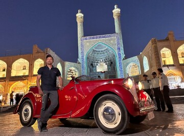 An Indian traveler poses for a photo during his visit to the UNESCO-registered Imam Square of Isfahan on September 9, 2023. His classic vehicle, a 1950 MG YT, is seen in the foreground as well.