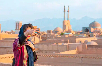 A domestic traveler takes a selfie with the 12th-century Jameh Mosque of Yazd seen in the background in the historical core of Yazd, which is a UNESCO World Heritage.