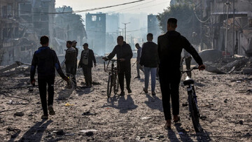 Men walk with bicycles through debris near the site of Israeli bombardment on a residential block in Jalaa Street in Gaza City on 14 January 2025 (AFP/Omar al-Qattaa)