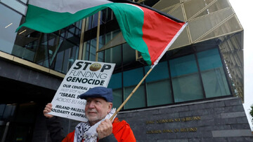 A man holds a sign and flag in support of Palestinians as he demonstrates outside the Central Bank of Ireland against the sale of Israel Bonds throughout the EU, in Dublin, Ireland, on 27 May 2025 (Cl