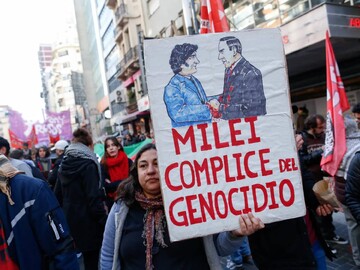 A woman holds a picket sign depicting President Javier Milei shaking hands with Israeli Prime Minister Benjamin during protests in Buenos Aires, Argentina, on August 9 [Francisco Loureiro/Reuters]