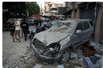 People pass a damaged car at the site where an Israeli strike hit an apartment building in Dahiyeh in the southern suburb of Beirut, Sunday, November 23, 2025 [Bilal Hussein/AP Photo]