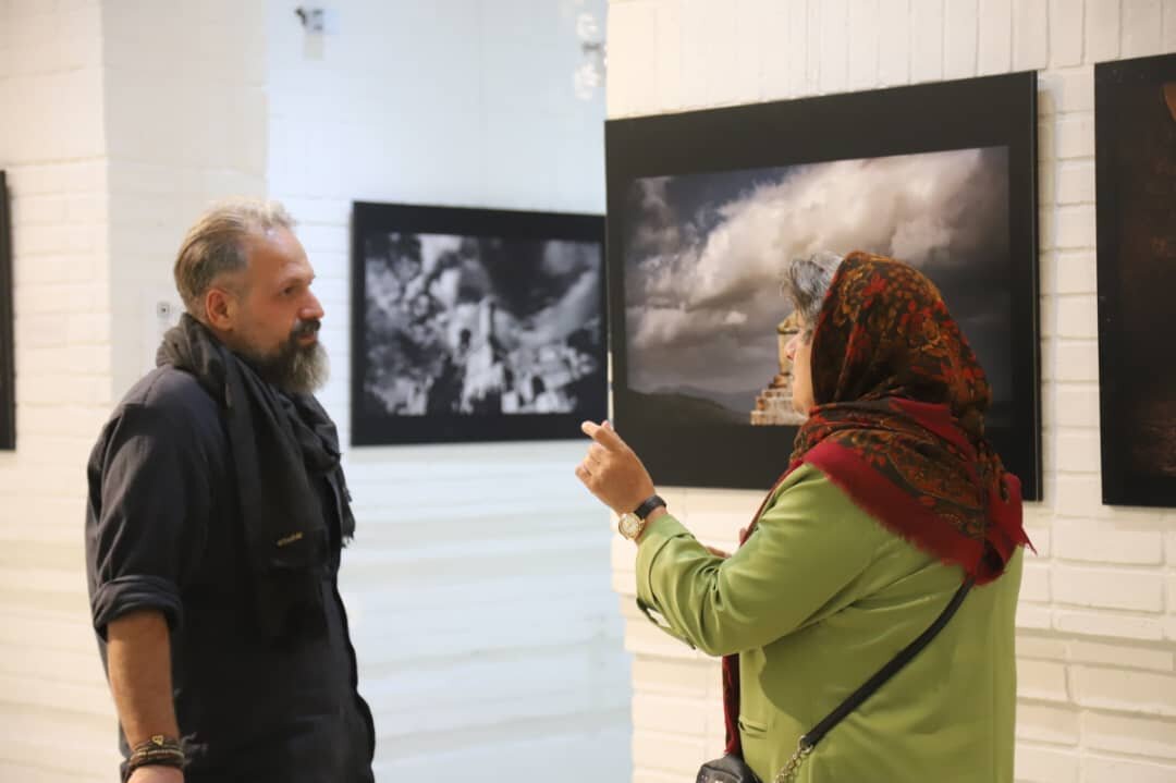Photographer and cultural heritage researcher Herbert Karim-Masihi (L) speaks with a visitor at an exhibition of his selected works at the Sa’dabad Cultural-Historical Complex in northern Tehran, December 4, 2025.