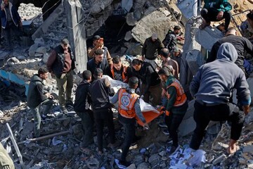Rescuers carry the body of a victim amid the debris of Sheikh Radwan police station in Gaza City following an Israeli air raid [AFP]