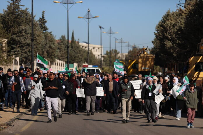 People, holding banners and flags, gather in the Syrian city of Qunaitra to protest Israeli military actions on December 19, 2025. (Izz Aldien Alqasem / Anadolu Agency)