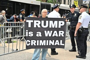 While Trump was addressing the UN General Assembly in New York, a protestor holds a placard saying "Trump is a war criminal"