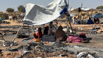 Displaced Sudanese people who fled el-Fasher after its fall sit in the shade amid the remains of a fire at a camp in Tawila on 11 February 2026 (AFP)